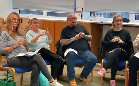 A group of people sitting down and learning BSL Level 1 course - following the British Sign Language signs after the tutor.