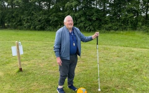 An older man holding a cane and standing near a yellow-neon ball