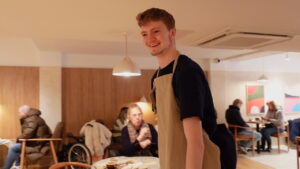 A young man wearing an apron walking around the tables at a café