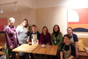 Seven people posing and looking at the camera standing around a table in a cafe