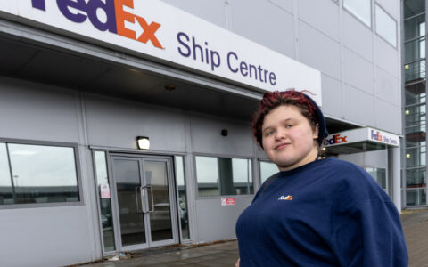 A person standing if front of a big sign on a building saying 'FedEx' Ship Centre