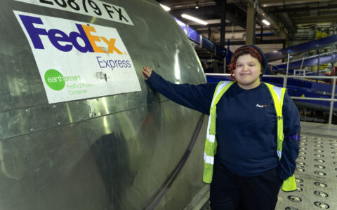 A young person in high-vis jacket standing next to a metal tank with FedEx logo on it