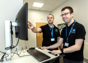 Two men in a Colchester Hospital uniform looking at a computer screen - one is pointing at it.