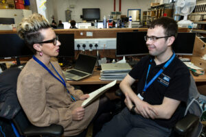 A young man and woman talking to each other while sitting down at their desks