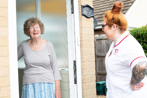 Older lady opening her front door to welcome an ECL member of staff in a white tunic.