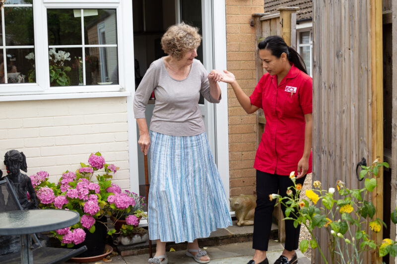 Older lady being guided outside of her house and into her back garden by an ECL Community Care Assistant.