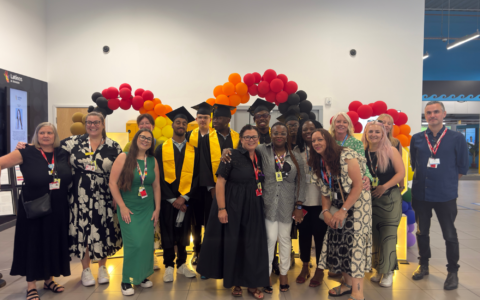 A group of people wearing graduation robes surrounded by staff