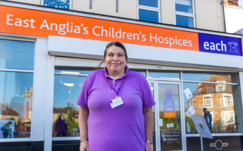 Elaine standing in front of the EACH charity shop with a volunteer badge