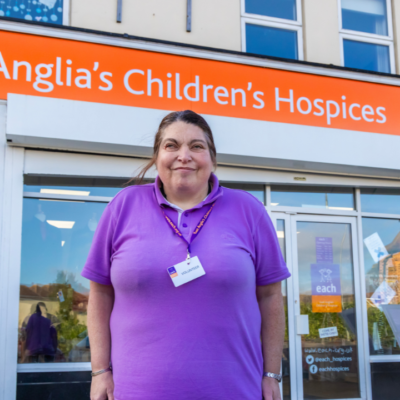 Elaine standing in front of the EACH charity shop with a volunteer badge
